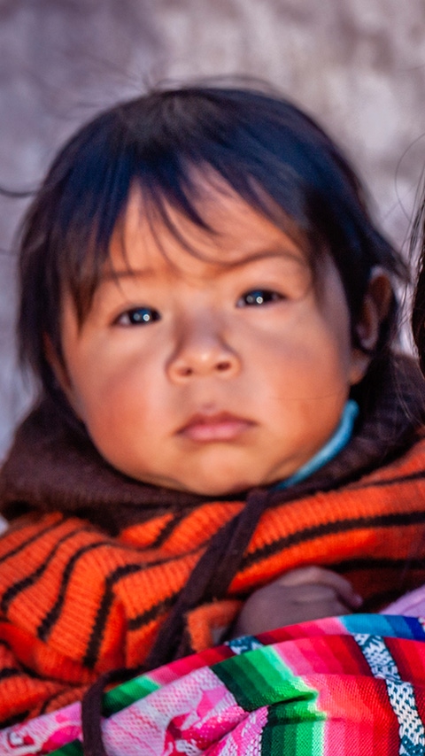 Young South American woman carries a toddler in a sling on her back